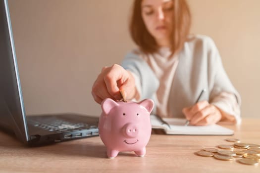 A young girl makes calculations, checks her finances, makes notes in a notebook and sets aside some of the funds, savings in a piggy bank for personal expenses and future development.