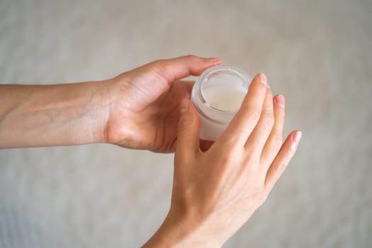 Young female hands hold a jar of moisturizing cream to maintain health, softness of the skin, the woman takes care of her health and beauty.