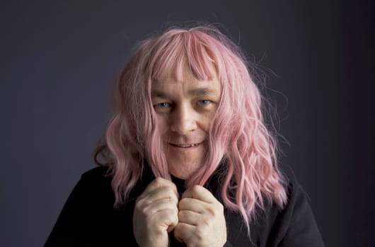 Portrait of a man who tried on a pink wig, looks at the camera, grimaces, poses. Close-up.