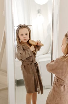 A girl in a brown coat looks through a large mirror at the camera.