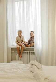 A boy and a girl in bathrobes are sitting on the windowsill, talking, playing.