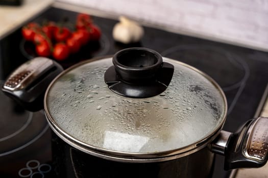 condensation drops on the transparent glass lid of the kitchen pot boiling on the stove. Close up. the misted lid of a pot of boiling water. Moist condensation from boiling water on the transparent glass lid of the kitchen pan while cooking