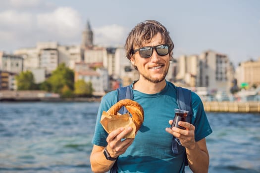 Man in Istanbul having breakfast with Simit and a glass of Turkish tea. Glass of Turkish tea and bagel Simit against golden horn bay and the Galata Tower in Istanbul, Turkey. Turkiye.