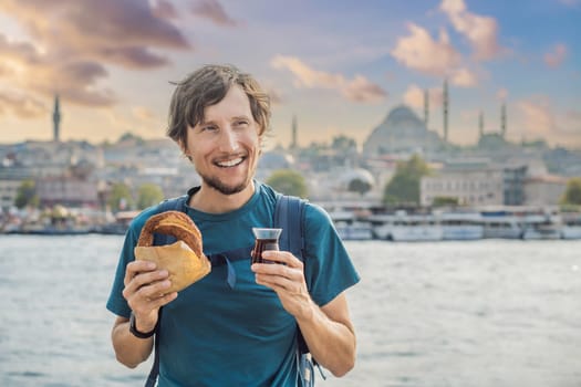 Man in Istanbul having breakfast with Simit and a glass of Turkish tea. Glass of Turkish tea and bagel Simit against golden horn bay in Istanbul, Turkey. Turkiye.