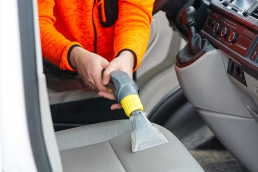 Handyman vacuuming car front textile seat with vacuum cleaner. man cleaning work Minivan.