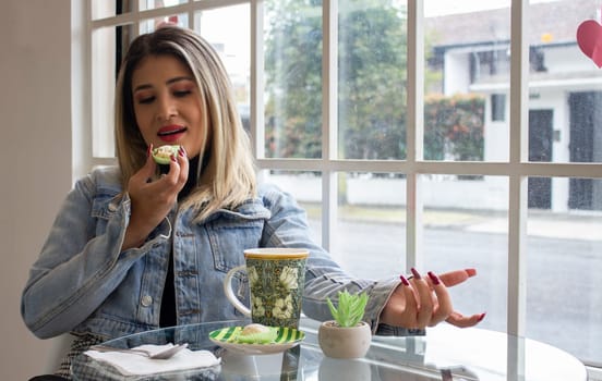 blonde woman eating a cake and having a coffee by the window of a cafeteria. High quality photo