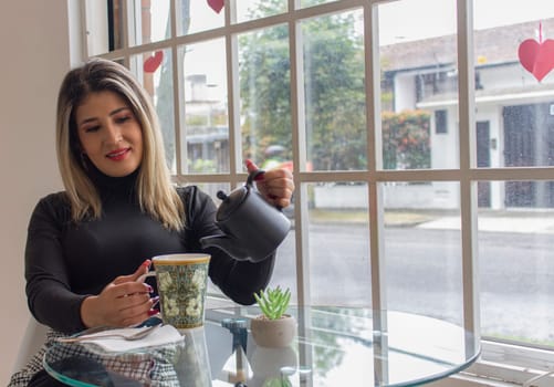 a young blonde woman pouring herself some tea with a smile on her face. High quality photo