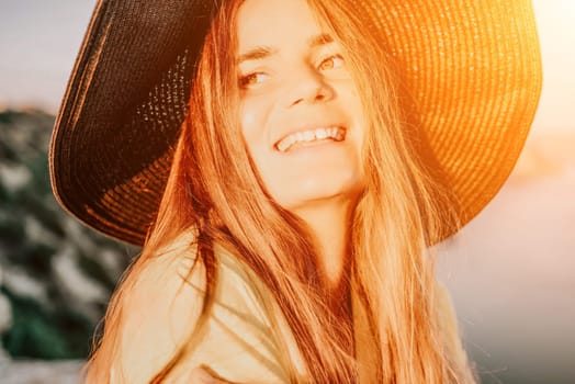 Portrait of happy young woman wearing summer black hat with large brim at beach on sunset. Closeup face of attractive girl with black straw hat. Happy young woman smiling and looking at camera at sea