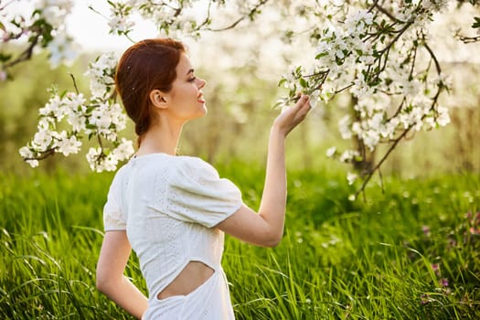 Young attractive woman with straight long hair standing in flowering Apple orchards. Beauty smiling woman looking at white flower. High quality photo