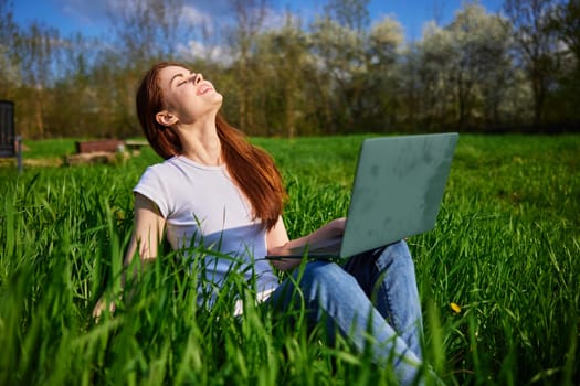on a clear sunny day, a happy woman works sitting at a laptop in the field. High quality photo