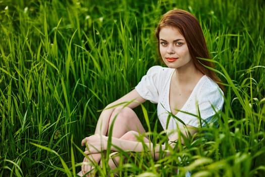 adorable, smiling woman sitting in nature relaxing in tall grass looking at camera. High quality photo