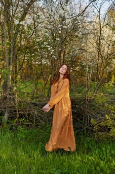 an elegant, sophisticated woman poses relaxed standing near a wicker fence at the dacha in a long orange dress. High quality photo