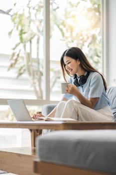 girl wearing headphones watching movies listening to music on laptop on the sofa at home on vacation with a cup of coffee..