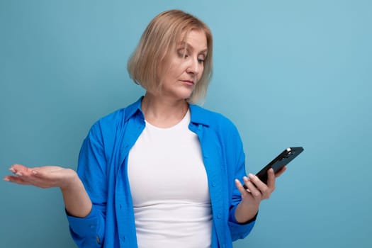 a woman of mature years makes a payment from a smartphone on a blue background copy space.