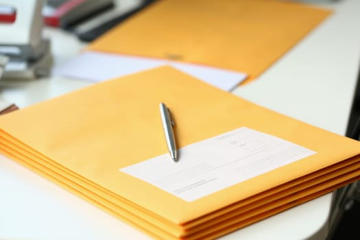 Yellow envelope with business correspondence with pen on desktop in office. Sending bank notices and letters to partners