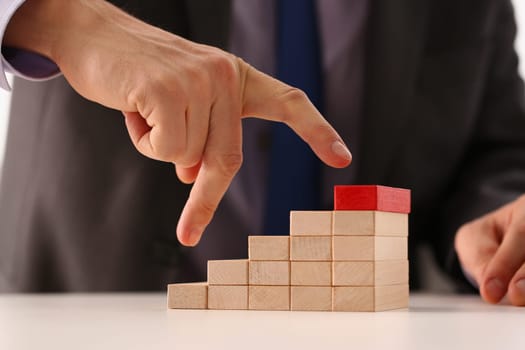 Man hand raises fingers up a wooden staircase made of wooden blocks. Successful career leader and achievement of business goals