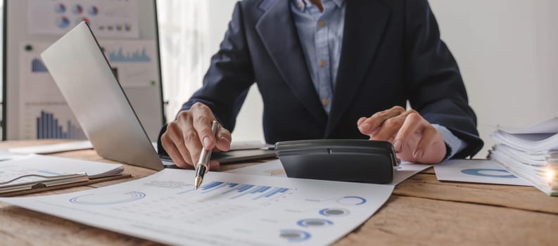 Close up Businessman using calculator and laptop for do math finance on wooden desk in office and business working background, tax, accounting, statistics and analytic research concept...