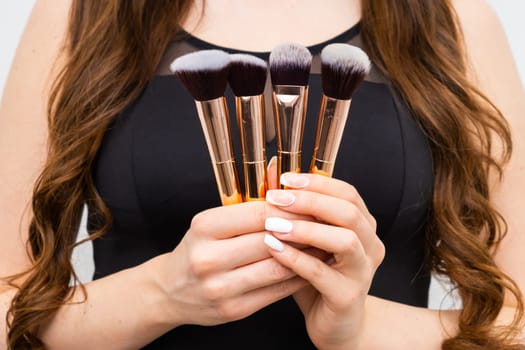 Close up in golden makeup brushes in woman hands with long hair.