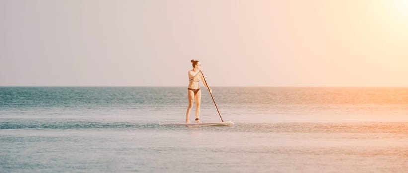 Sea woman sup. Silhouette of happy middle aged woman in rainbow bikini, surfing on SUP board, confident paddling through water surface. Idyllic sunset. Active lifestyle at sea or river