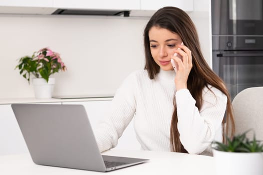 Woman has a call using smartphone while working with laptop at home.