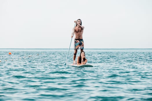 Silhouette of woman standing, surfing on SUP board, confident paddling through water surface. Idyllic sunset or sunrise. Sports active lifestyle at sea or river.