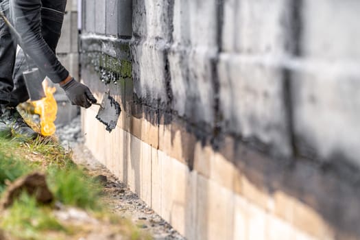 installation of asphalt insulation on the wall of the building with trowel.