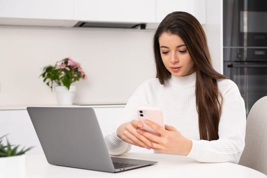Woman texting using smartphone while working with laptop at home.