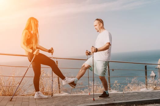 Happy Middle aged couple or friends practicing nordic walking in park near sea. Mature couple with trekking poles walking, practicing Nordic walking outdoors. Aging youthfully and sport concept.