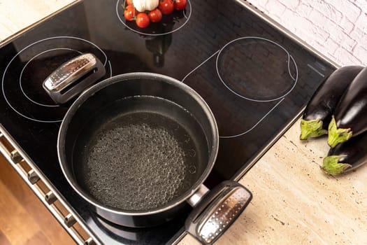 a pot of boiling water on an electric stove in the kitchen. ingredients for cooking dinner. tomatoes, eggplant and garlic