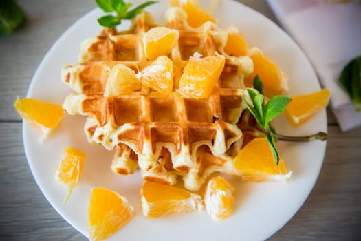 Cooked sweet Belgian waffles with oranges on a wooden table.