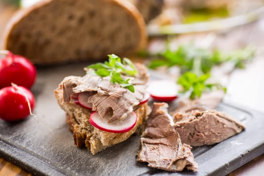 sandwich with baked meat, radish and herbs on a wooden table.