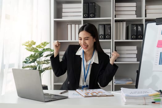 business asian woman triumphing in office happy excited successful Portrait of a cheerful Asian businesswoman sitting at the table in office.