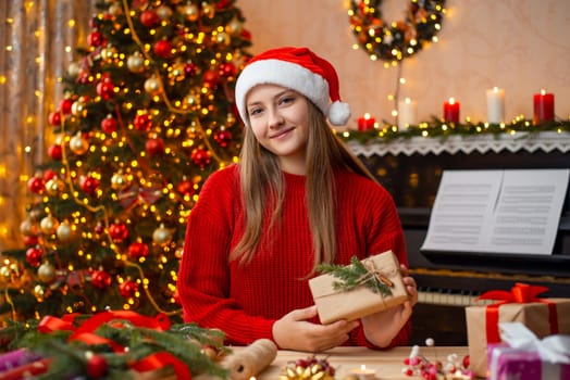 Happy young girl sitting near the table and holding packed and decorated present box