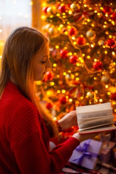 Girl reading a book near gorgeous Christmas tree with warm yellow lights on it