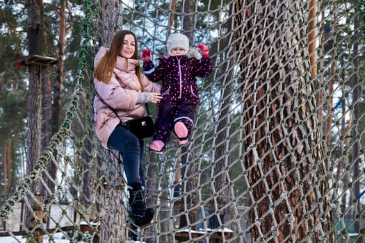 a large public green area in a town, used for recreation.Cheerful mother with a child on a playing net stretched on trees in winter park.