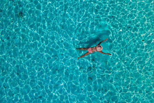 women swimming in the ocean of Koh Kradan Island with a white tropical beach and turqouse colored ocean. women in blue ocean seen from above with a drone