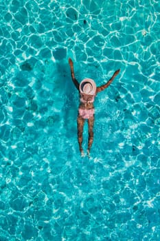 women swimming in the ocean of Koh Kradan Island with a white tropical beach and turqouse colored ocean. women in blue ocean seen from above with a drone