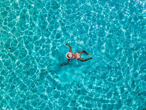 women swimming in the ocean of Koh Kradan Island with a white tropical beach and turqouse colored ocean. women in blue ocean seen from above with a drone