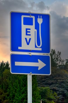 EV charging station road sign on dramatic clouds sky background