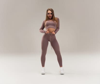 sexy athletic girl in a tight fitness tracksuit on a light background copy paste in studio