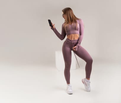 sexy athletic girl in a tight fitness tracksuit on a light background copy paste in studio