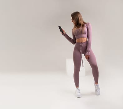 sexy athletic girl in a tight fitness tracksuit on a light background copy paste in studio