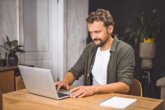 Modern freelancer lifestyle, man intently focused on laptop, sitting in cozy home office. Concept of working from home, emphasizing the freedom and flexibility that comes with being self-employed. High quality photo