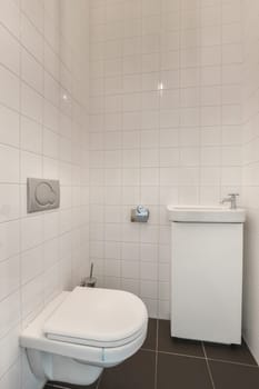 a white toilet in a bathroom with black tiles on the floor and wall behind it, there is a small trash can be seen
