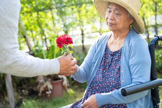 Asian senior or elderly old lady woman holding red rose flower, smile and happy in the sunny garden.