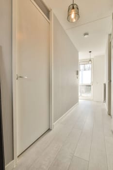 a long hallway with white walls and wood flooring on the right hand side, there is an open door leading to another room