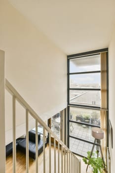 a living room with wood flooring and white walls, looking out onto the street from an upstairs stairwellway