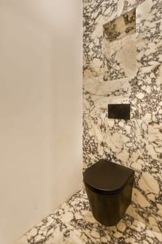 a bathroom with marble walls and black toilet in the corner, while it appears to be used for public use