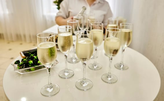 The waitress distributes sparkling white wine to the guests. A group of champagne glasses at a party.