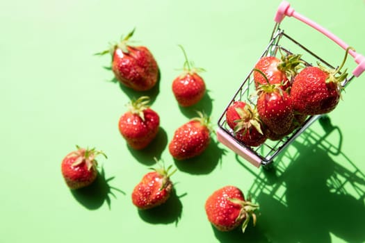 Little shopping cart filled with raw delicious strawberries. Concept shot symbolizing buying healthy food or ordering online